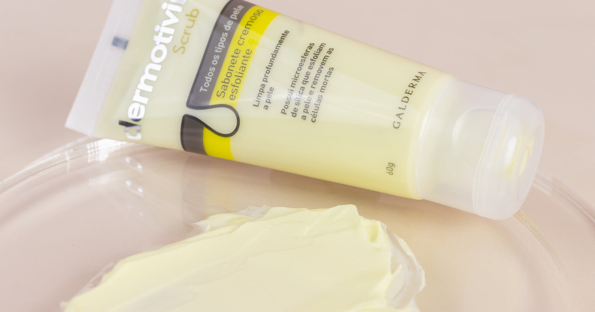 Um tubo de Dermotivin Scrub, um sabonete cremoso esfoliante para todos os tipos de pele, com uma amostra do produto em uma superfície transparente.