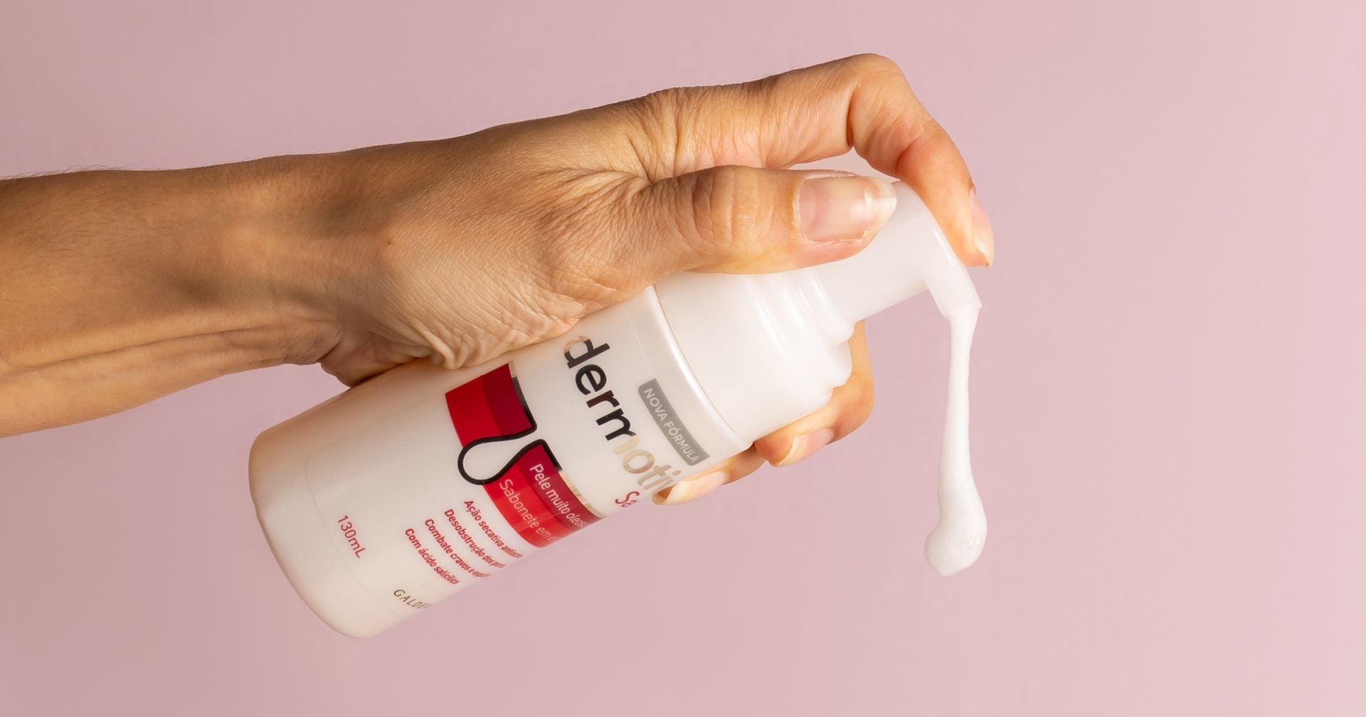 Uma mão segurando um frasco de produto para a pele da marca Dermotivin Oil Control, com espuma branca saindo do bico dosador. O fundo é amarelo, destacando o frasco e a textura do produto.