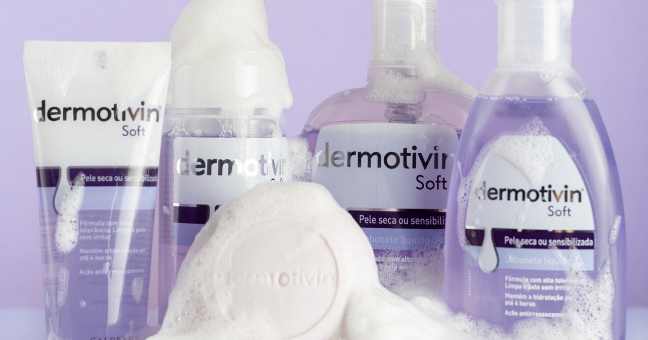 Linha completa Dermotivin Soft sobre fundo lilás, mostrando sabonete em barra, sabonete líquido e espuma de limpeza com embalagens brancas e detalhes roxos. Produtos especiais para pele seca ou sensibilizada com textura suave.