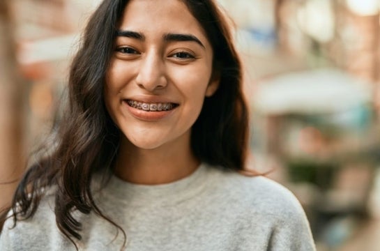 Adolescente branca usando aparelho dental e sorrindo.