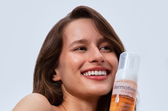 Mulher branca sorrindo e segurando a embalagem da espuma de limpeza Dermotivin Oil Control.